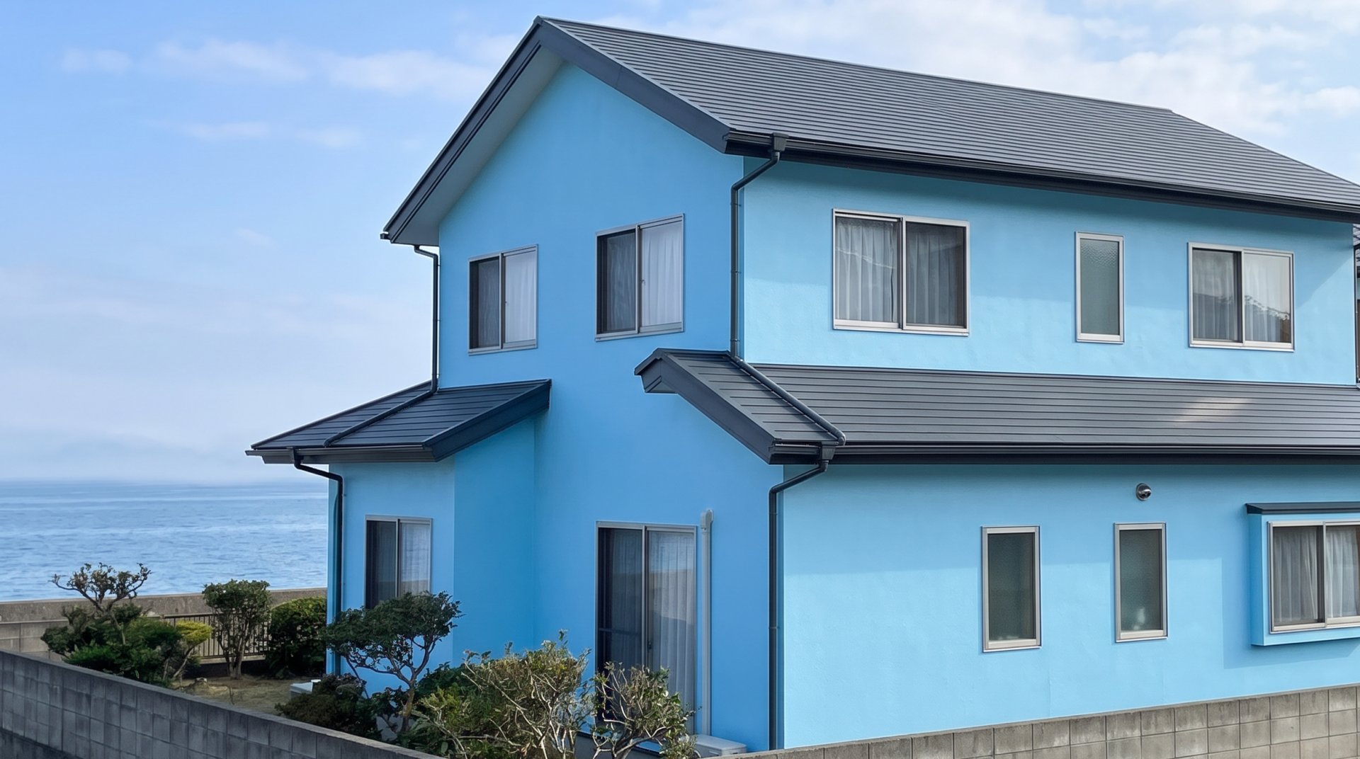 水色に塗り替えた2階建ての家と、うしろに見える海（見本の画像）