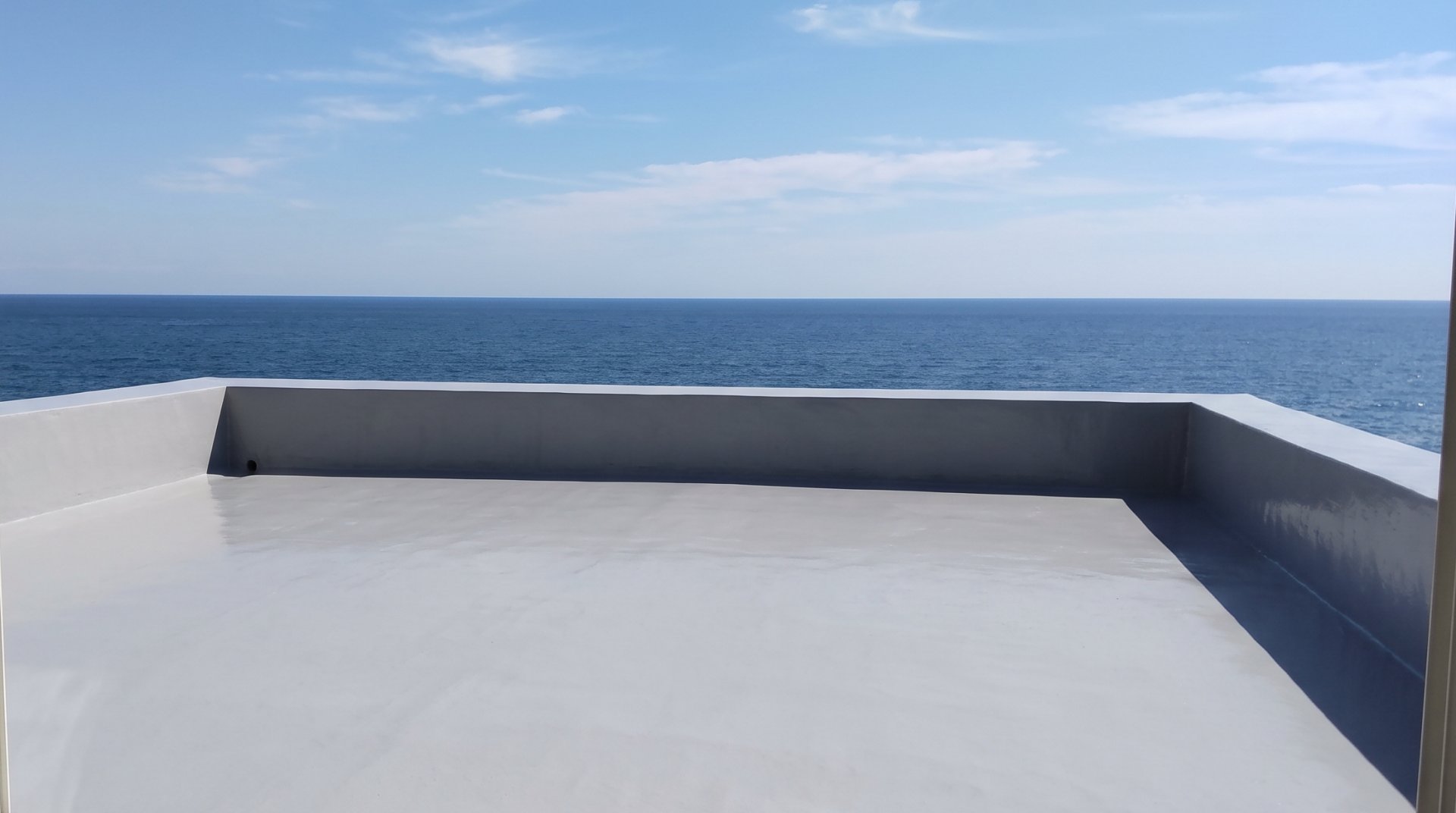 防水とトップコートを塗り終えたベランダの床と、手すり壁の向こうの海（見本の画像）